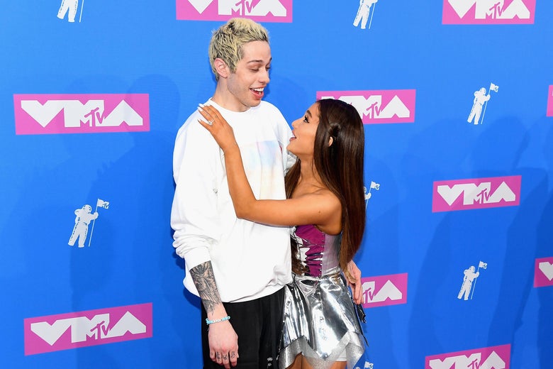 Pete Davidson and Ariana Grande stand together against a blue VMAs backdrop